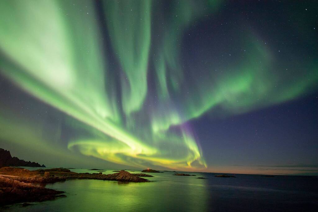 Aurore Boreali verdi danzanti nel cielo notturno sopra un tranquillo paesaggio marino norvegese.